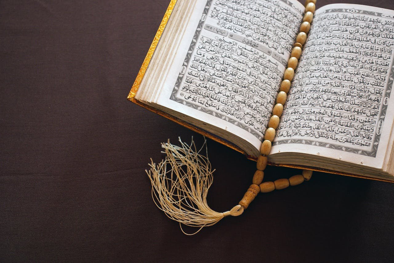 A Quran open to Arabic text with prayer beads resting on a brown surface, symbolizing Islamic faith.